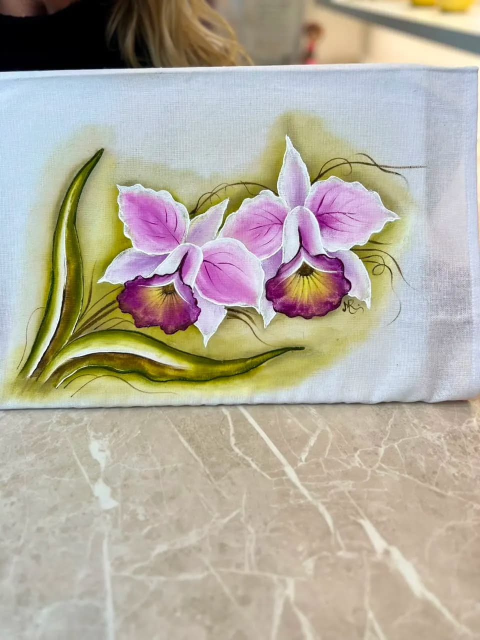 Close de um pano pintado com duas orquídeas lilás e folhas verdes