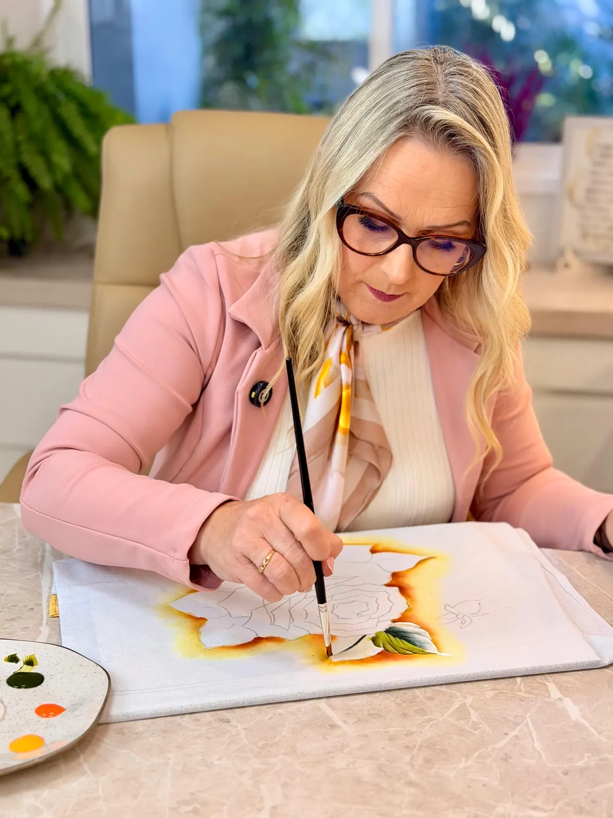 Marisa, de casaco rosa, pintando uma rosa em tecido